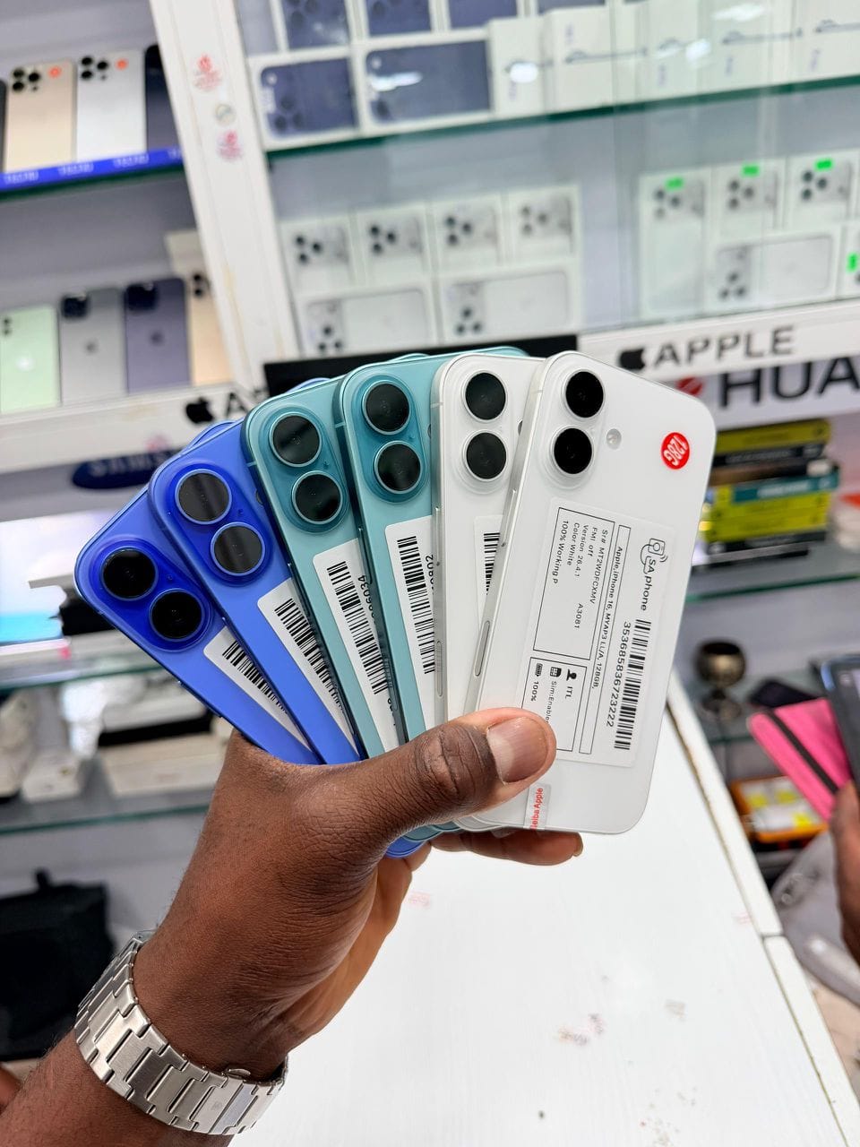 Six iPhone 16 bleus, sarcelle et blancs, vus de dos, tenus en main