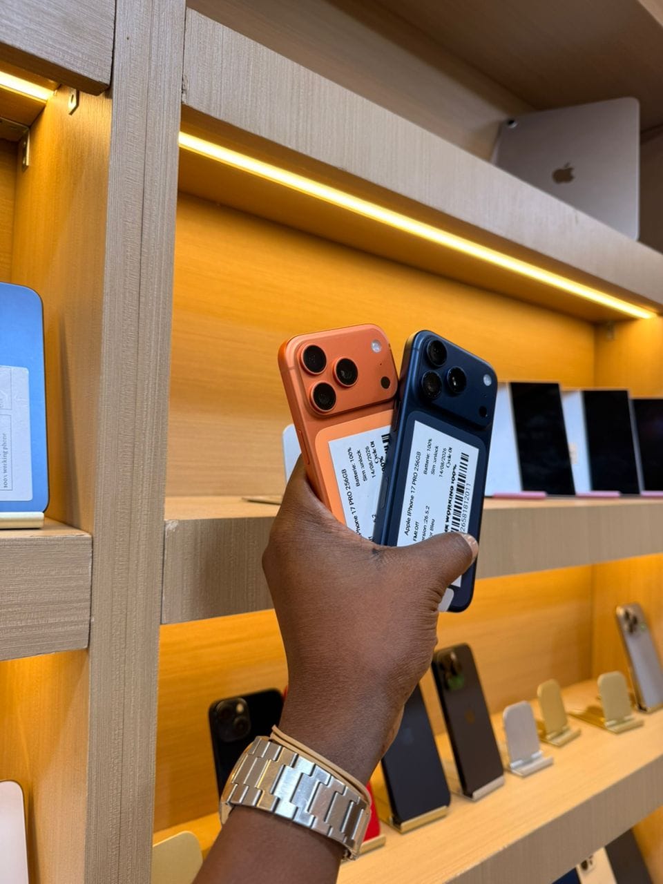 Deux iPhone 17 Pro, orange et bleu, vus de dos, tenus en main dans la boutique
