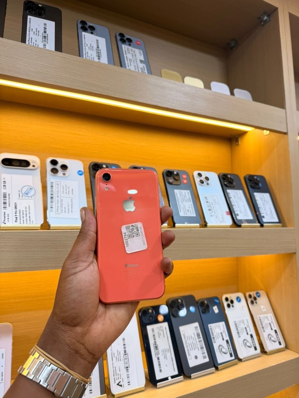 iPhone XR corail, vu de dos, tenu en main dans la boutique
